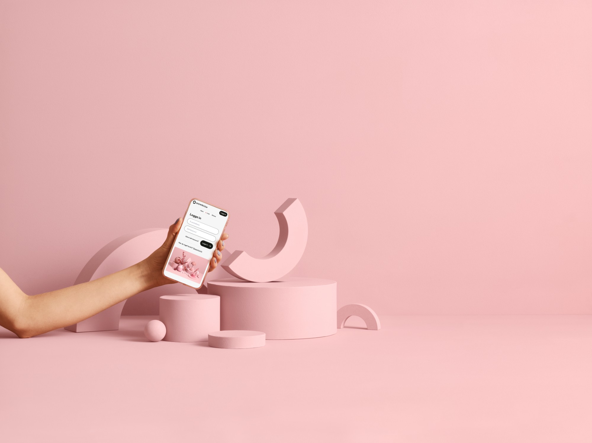 En hand håller en mobil med Showroom-appen framför rosa geometriska former