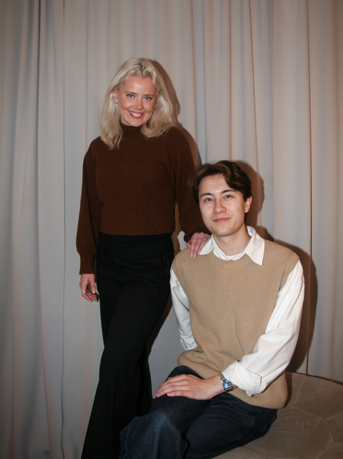 Frida standing with her hand on the shoulder of Isak, who is seated beside her